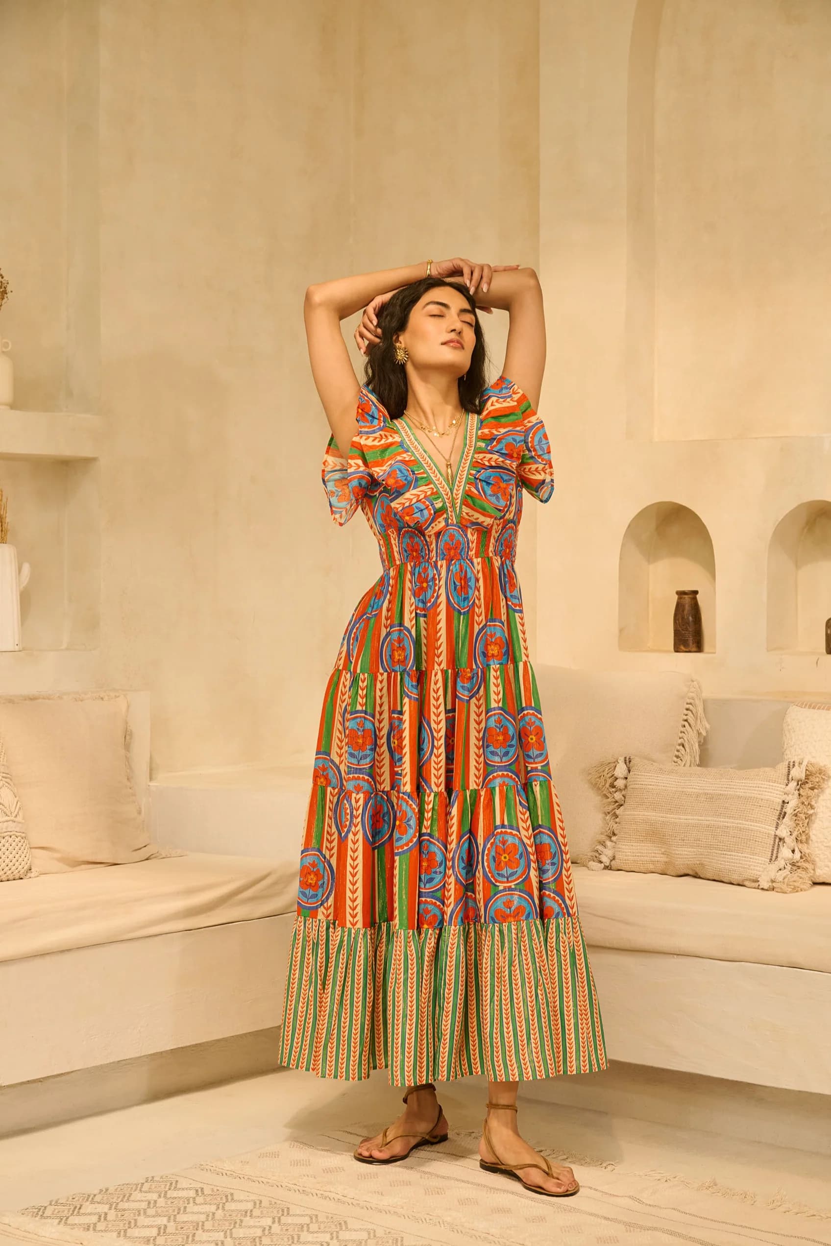 A printed tiered maxi in orange, blue and green against beige plaster